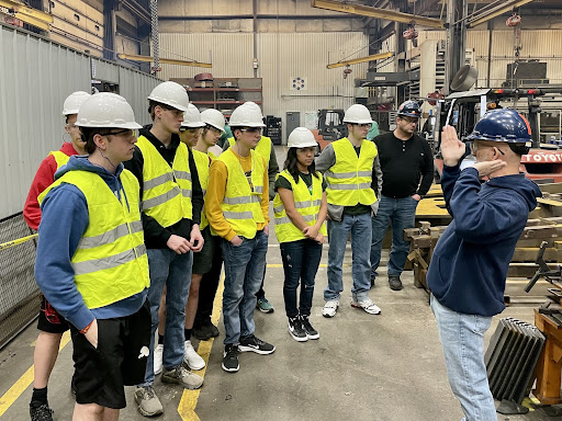 All members of both BotsIQ teams listen to their tour guide about the wonders of manufacturing